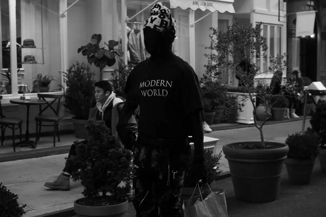 A street photograph of a man with a modern world shirt outside of Aime Leon Dore in Nolita